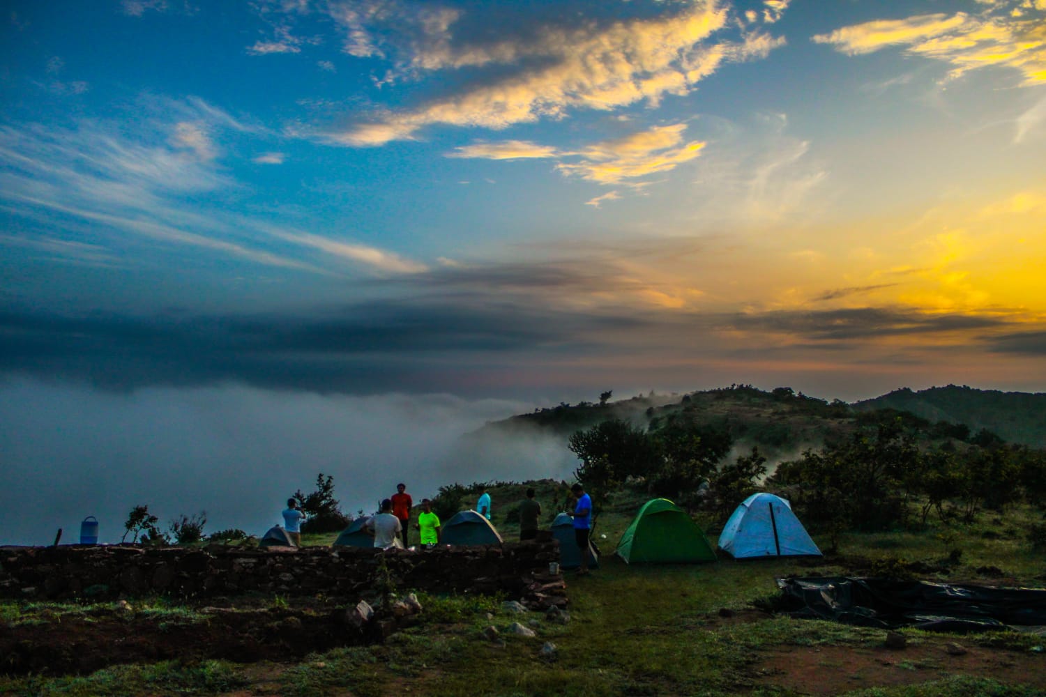 Tents pitched on an Aravali hilltop at sunset above a sea of clouds