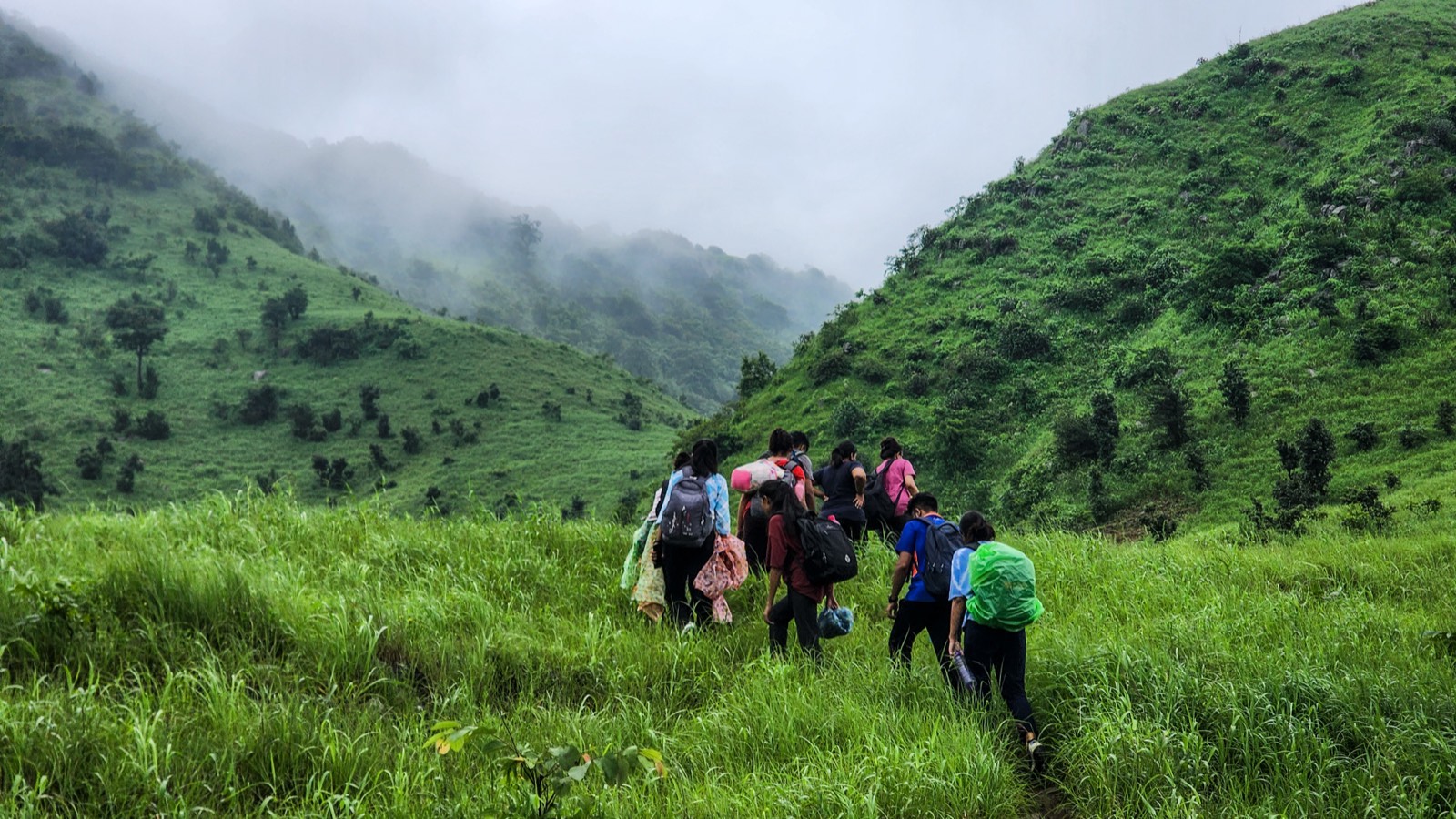 A group trekking up misty green Aravali hills with backpacks