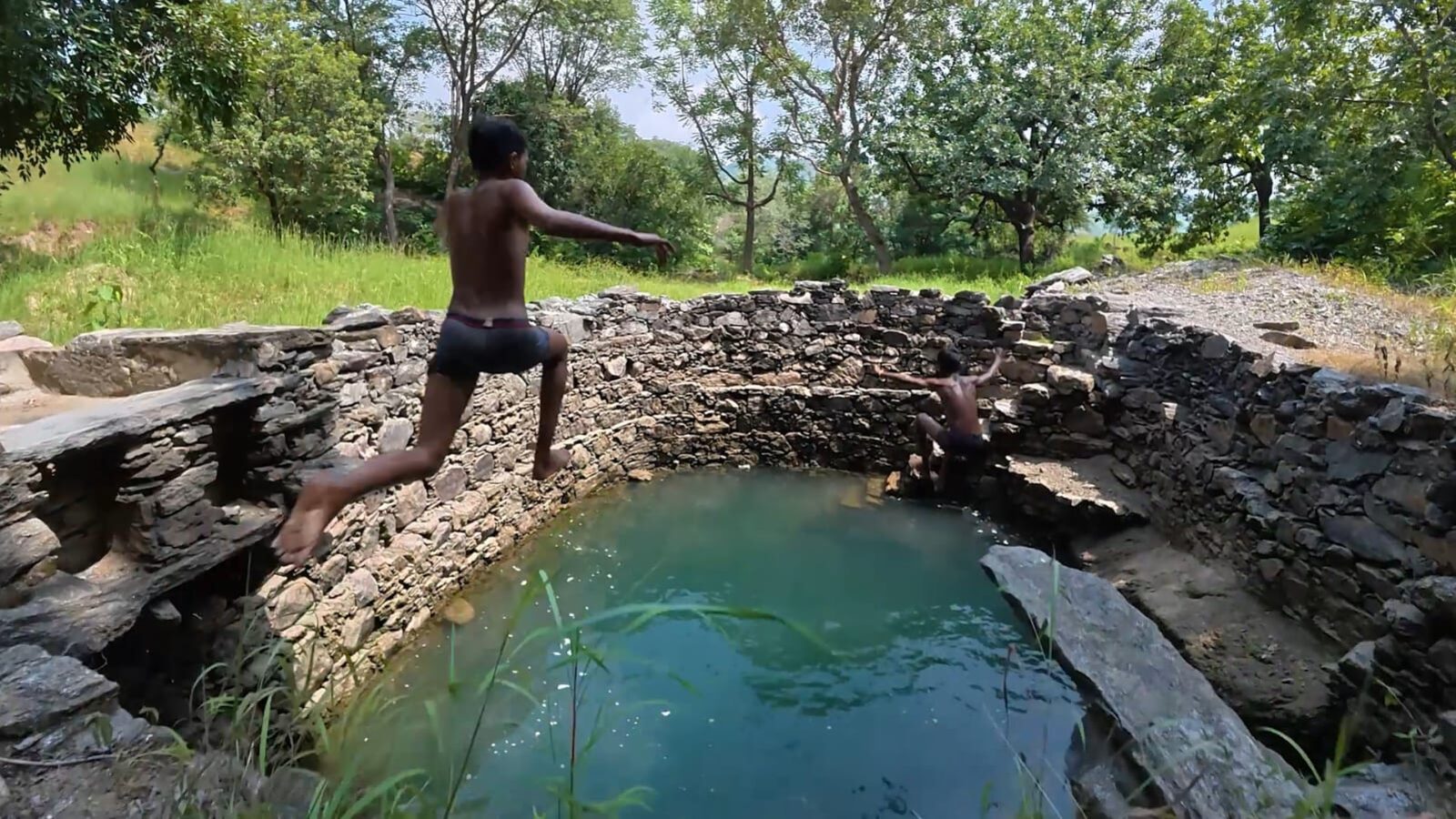 Village boys leaping into a traditional stone bavdi filled with green monsoon water