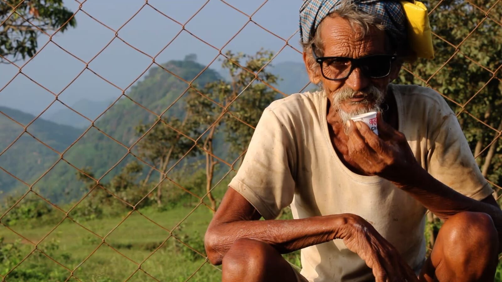 A shepherd resting with a cup of chai, mountains of the Aravali range rising behind him