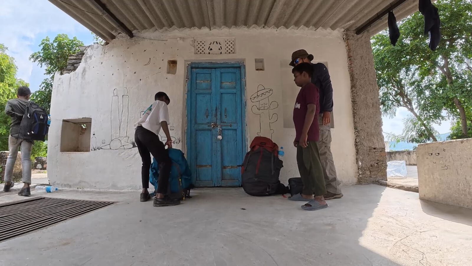 The boys and the trek leader packing rucksacks outside a village house with a blue door in Pasun