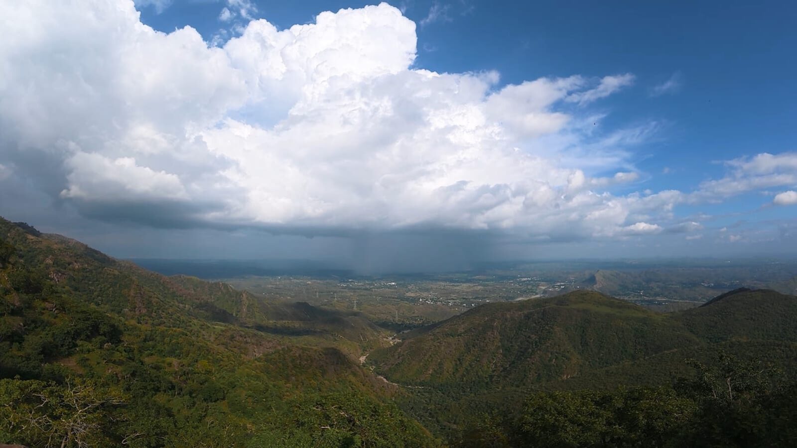View from the ridge of rain falling over distant Aravali mountains while sunlight falls nearby