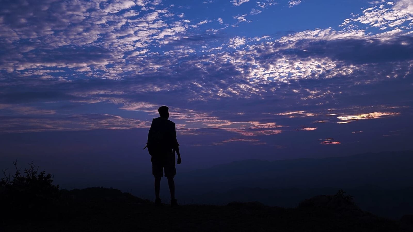 A lone figure standing at the summit campsite as the sun sets over the Aravali range